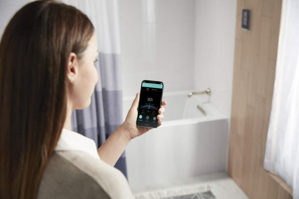 An over the shoulder shot of a woman using KOHLER PerfectFill smart bathing technology named a CES 2022 Innovation Award Honoree. she is facing a bathtub,