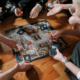 A group of family members gathered around, playing a board game together, laughing, and having a great time.