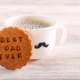 A close-up photo of a mug filled with steaming coffee and a delicious cookie with the words "Best Dad Ever" written on it, a perfect treat to celebrate Father's Day with PostFromUS.