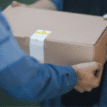 The hands of delivery personnel passing off a boxed package to a customer.