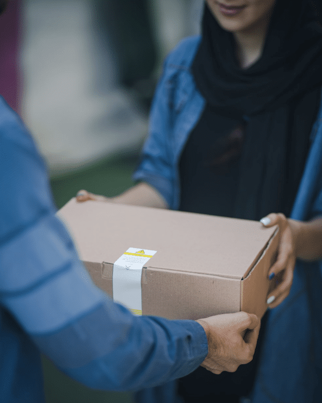 The hands of delivery personnel passing off a boxed package to a customer.