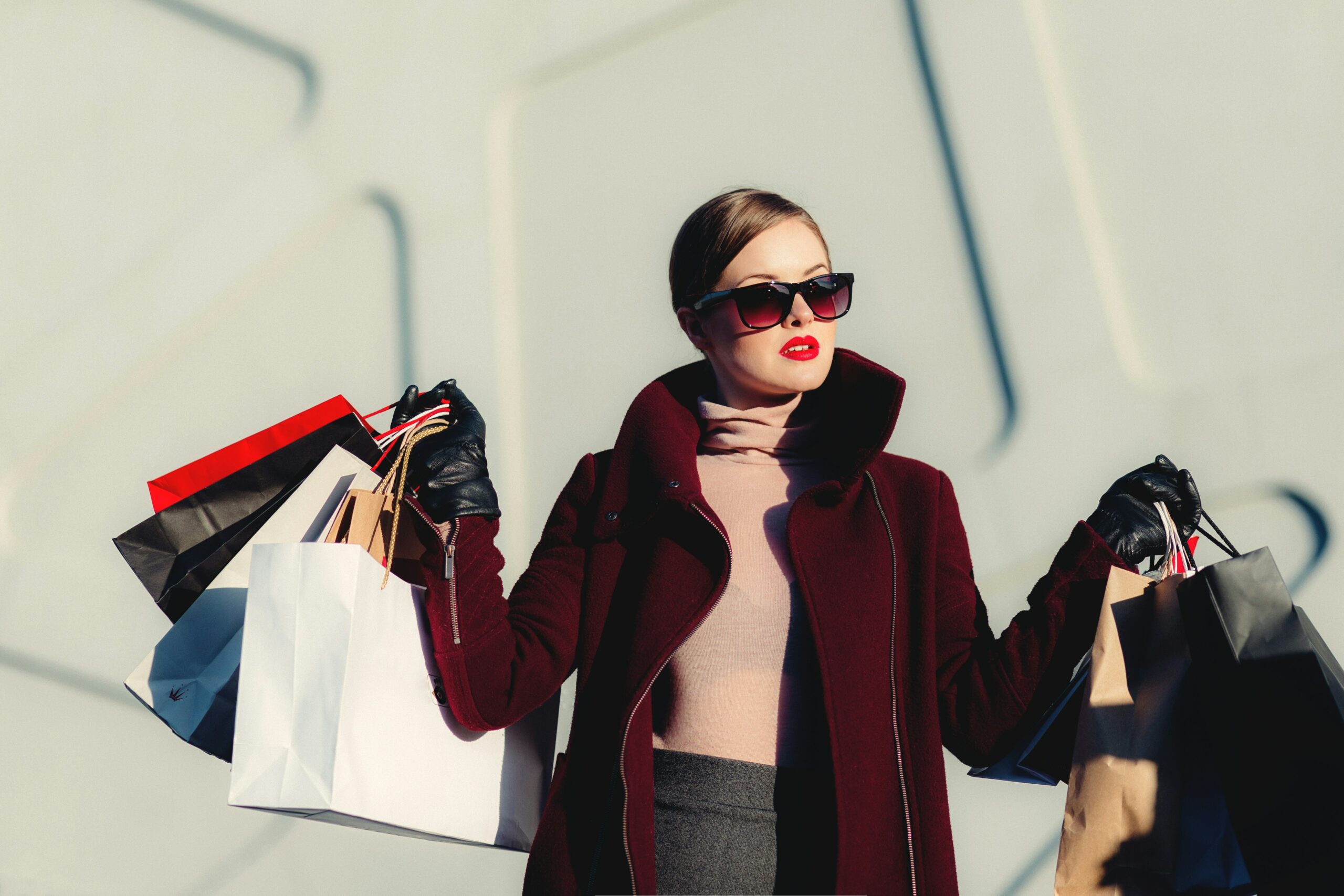A fashionable woman wearing sunglasses is holding shopping bags outside of a mall.