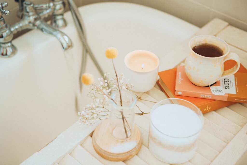 A candle is placed over a bath with a cup of tea and some flowers.