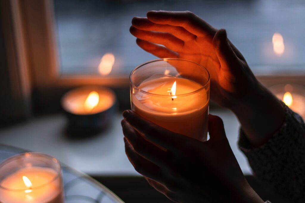 Bath and Body Works candles are lit. Someone is holding the one in focus, warming their hand.