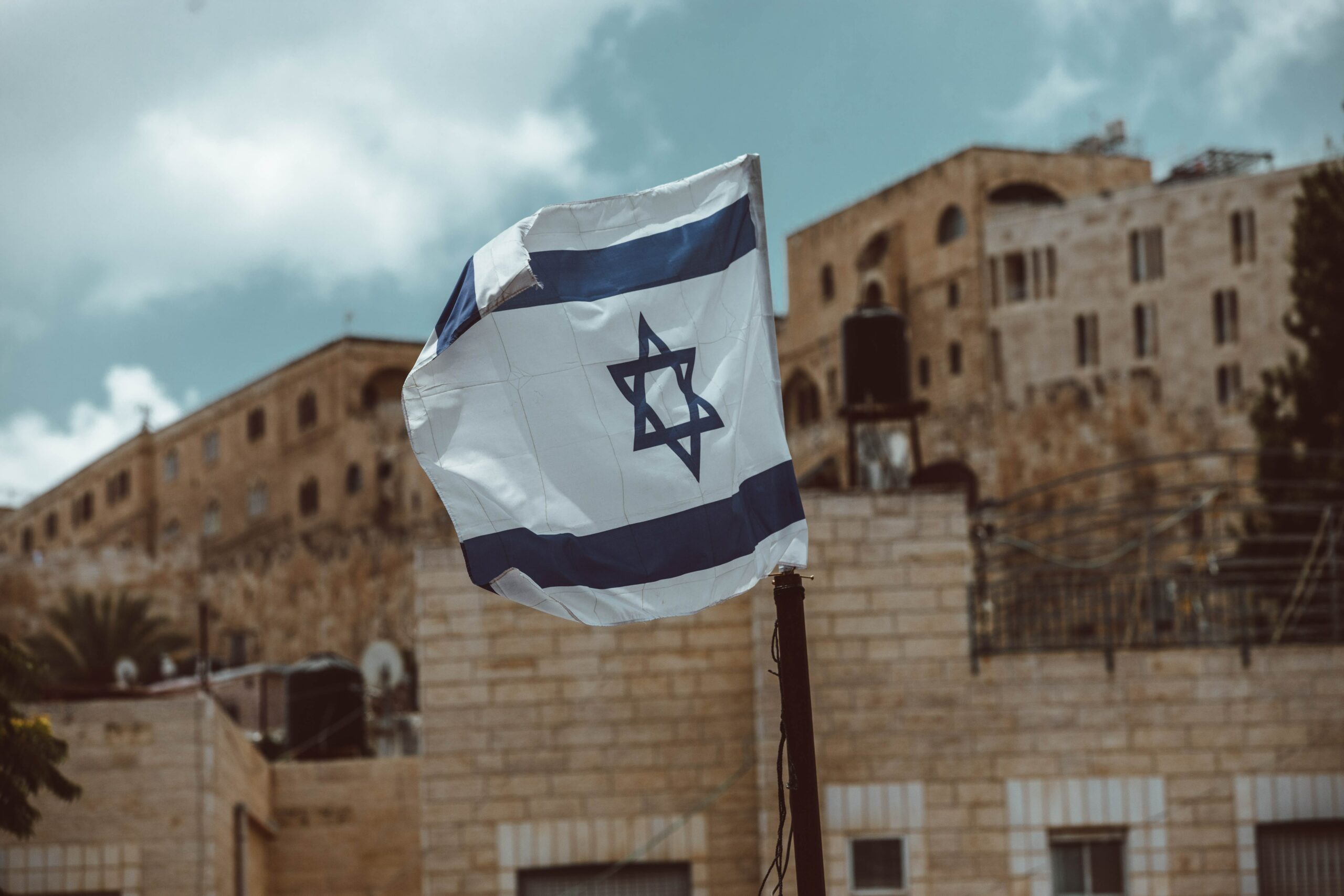 The Israeli flag waving in the wind from a flagpole.