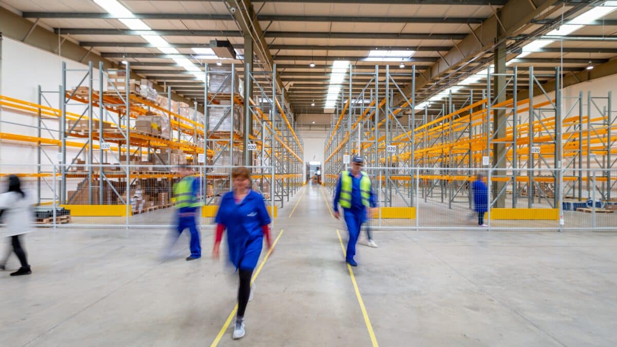 The inside of a California warehouse. There are large shelves and several workers moving about.