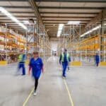 The inside of a California warehouse. There are large shelves and several workers moving about.