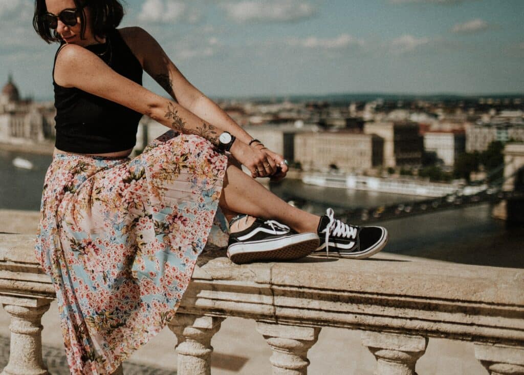 A woman is sitting on a railing in a European city, wearing Vans Old Schools.
