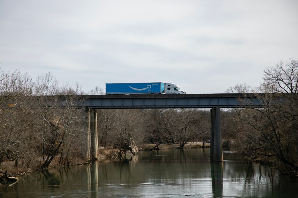 An Amazon shipping truck is moving across a bridge over water. 
