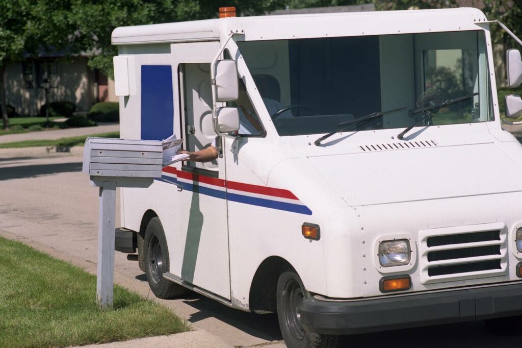 A USPS truck delivering mail into a mailbox right from the window. 