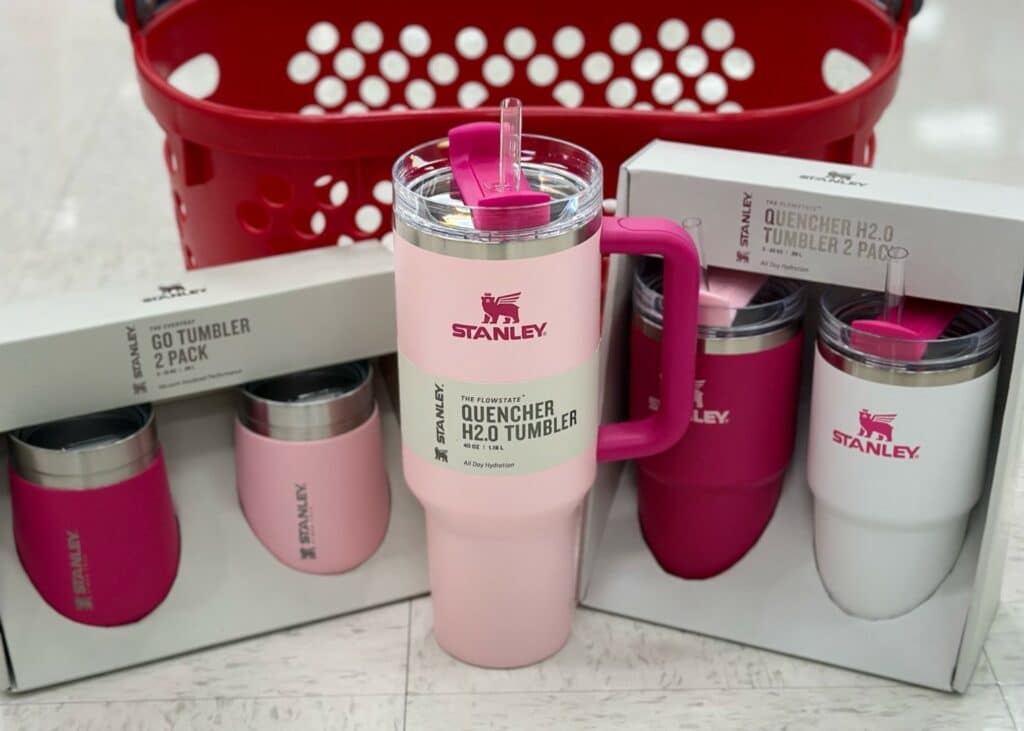 Two boxes of pink Stanley cup quenchers and a tumbler in the middle. They are placed on a floor in front of a shopping basket, likely in a Target shop.