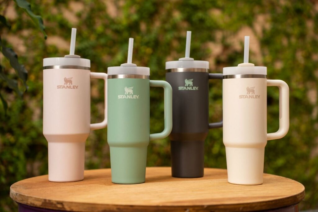 A set of four different colours of Stanley Cup Quencher are on a wooden table outside.