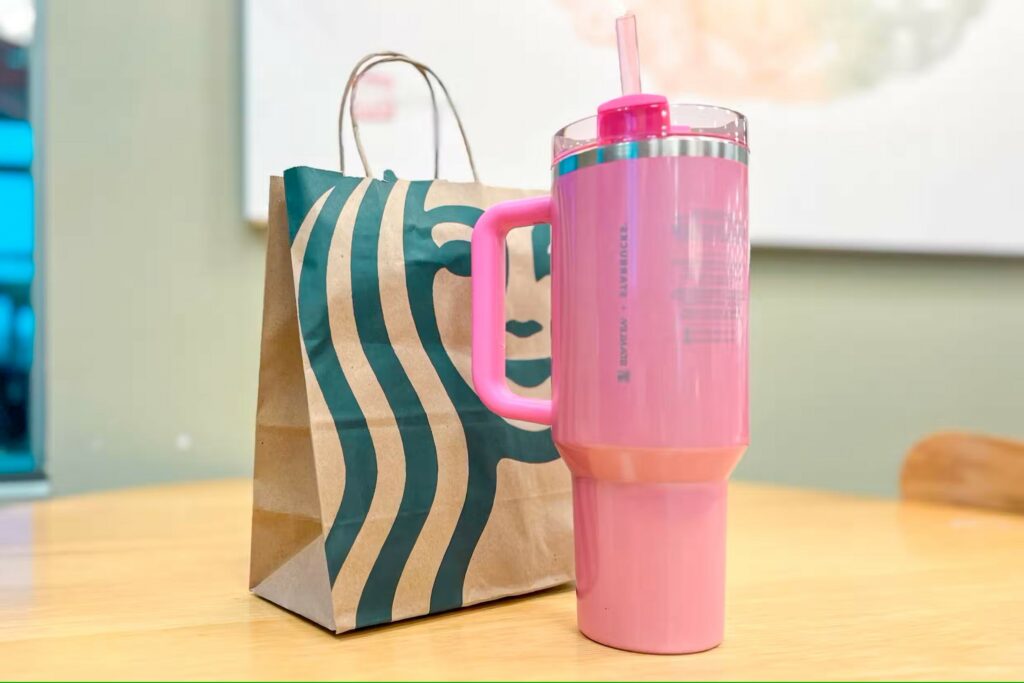 A pink stanley cup in front of a starbucks takeout bag