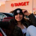 A girl is sitting in a shopping cart outside of a Target store.