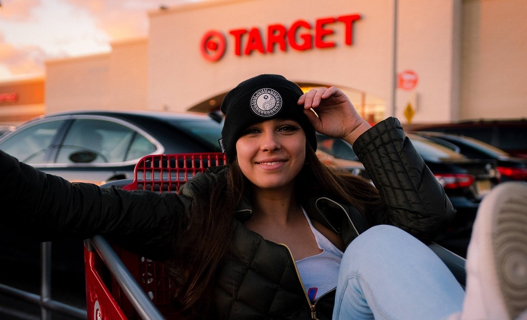 A girl is sitting in a shopping cart outside of a Target store.