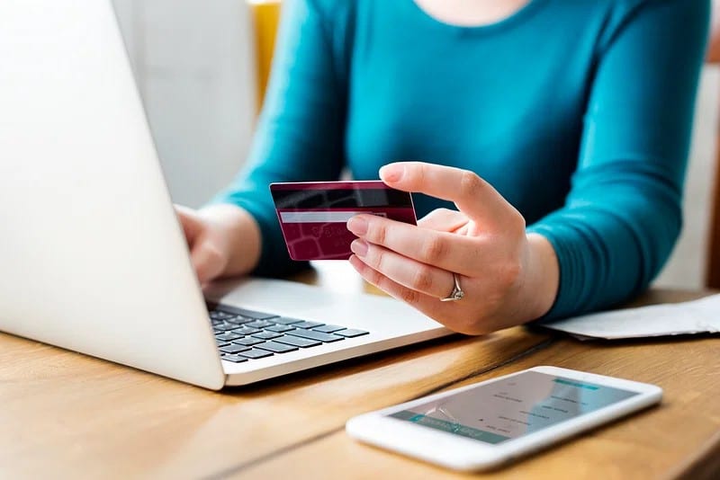 a lady with a blue shirt holds up her credit card as she goes to purchase a thumb hole hoodie shipped to uk