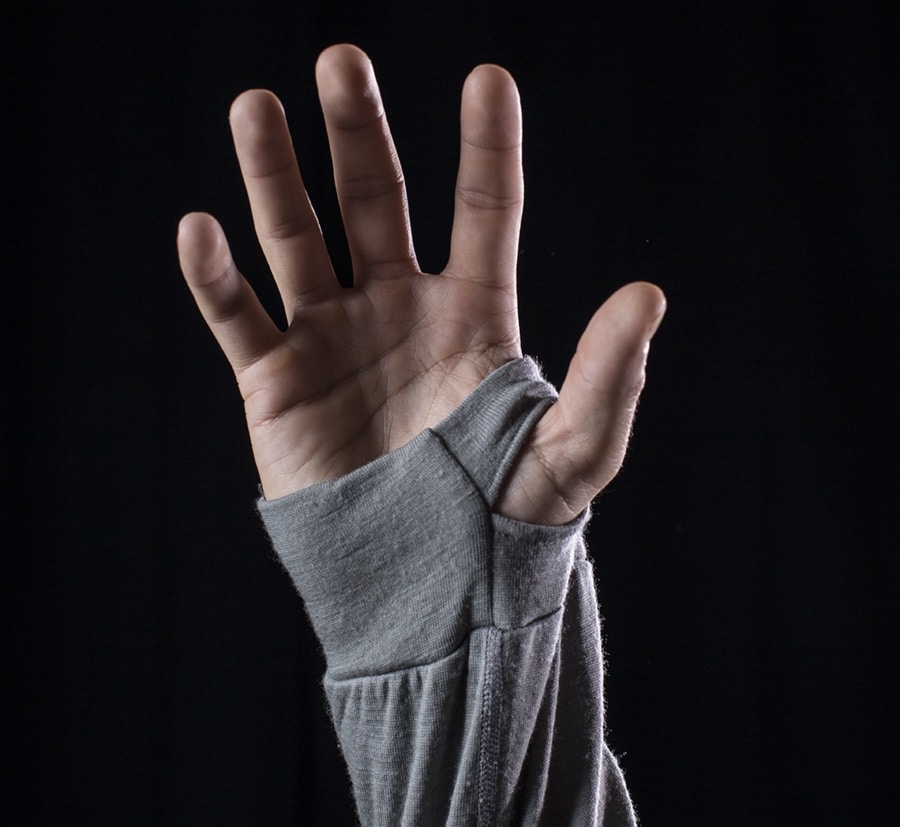 a large hand is spread out, with its thumb sticking through a thumb hole hoodie