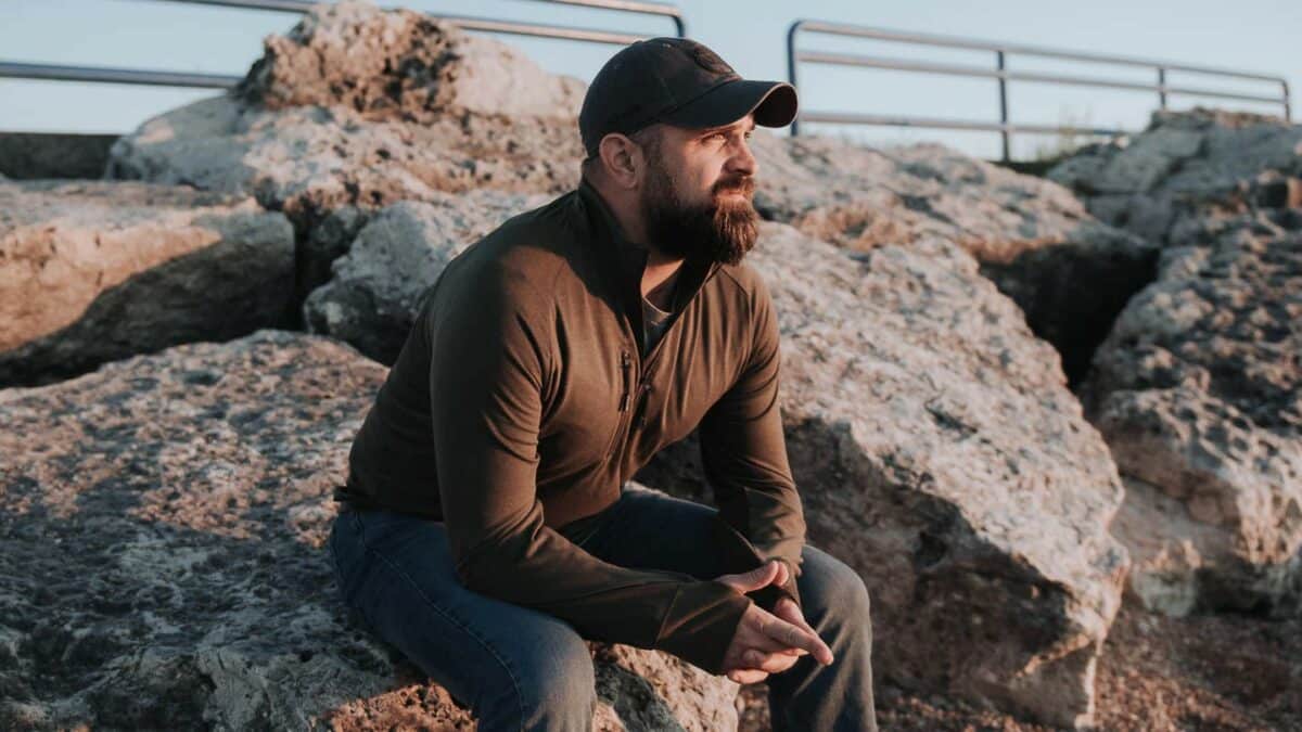 a man is sitting on a rock outside, wearing a thumb hole hoodie