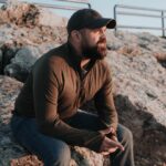 a man is sitting on a rock outside, wearing a thumb hole hoodie