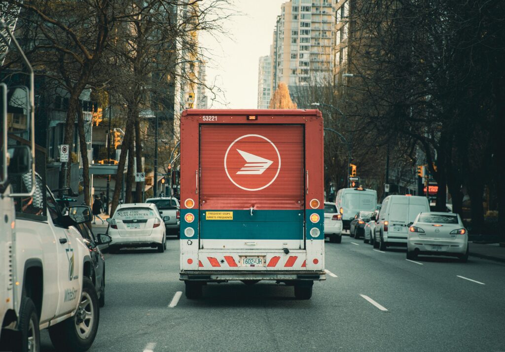 The back view of a Canada Post delivery van as it drives down a city road.