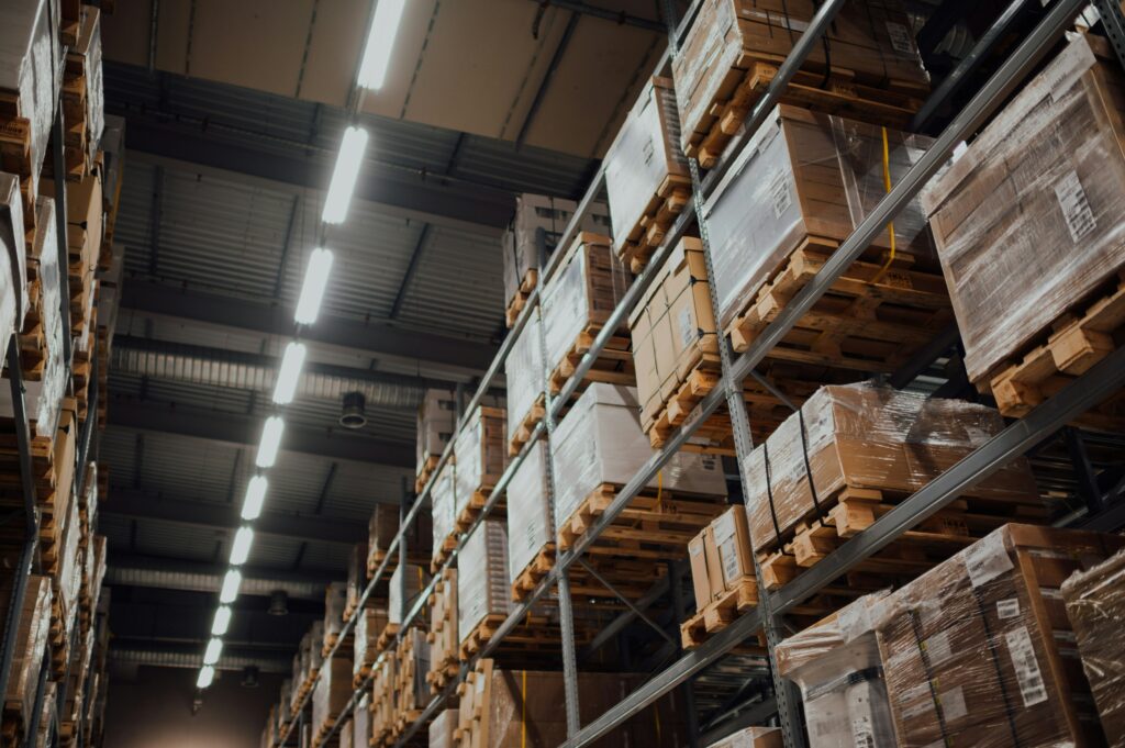 A view from below of tall shelves inside a shipping warehouse. Large crates for shipping electronics are wrapped in plastic.