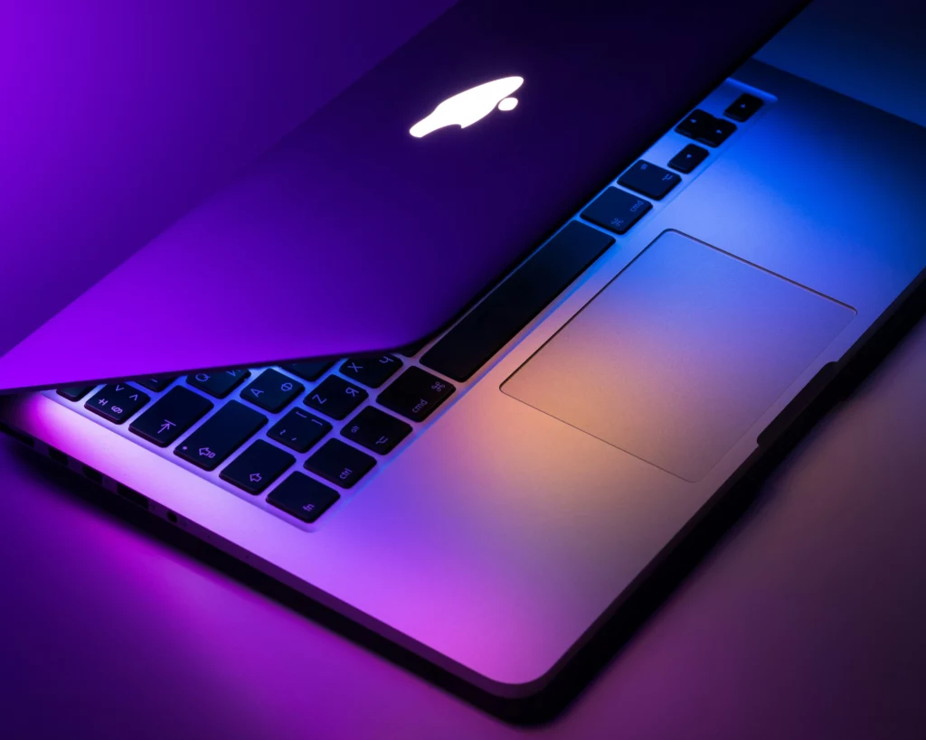 흰색 책상 위에 분홍색과 파란색 조명이 비추는 Apple Macbook Pro는 미국에서 출시된 노트북입니다.