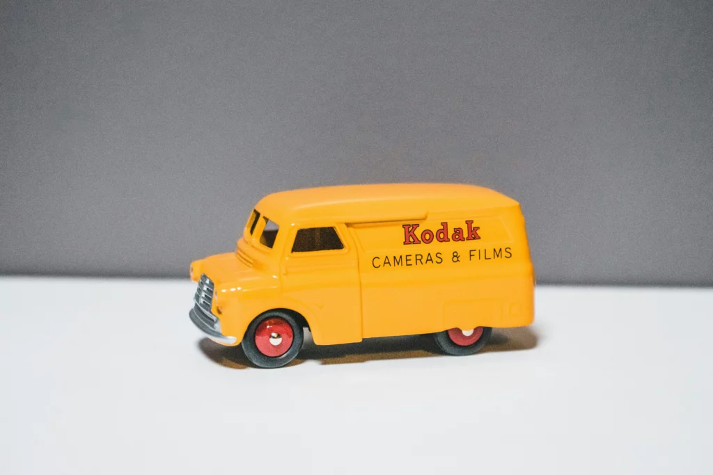 Una furgoneta Kodak amarilla de una colección de coches modelo sobre una mesa blanca con fondo gris.