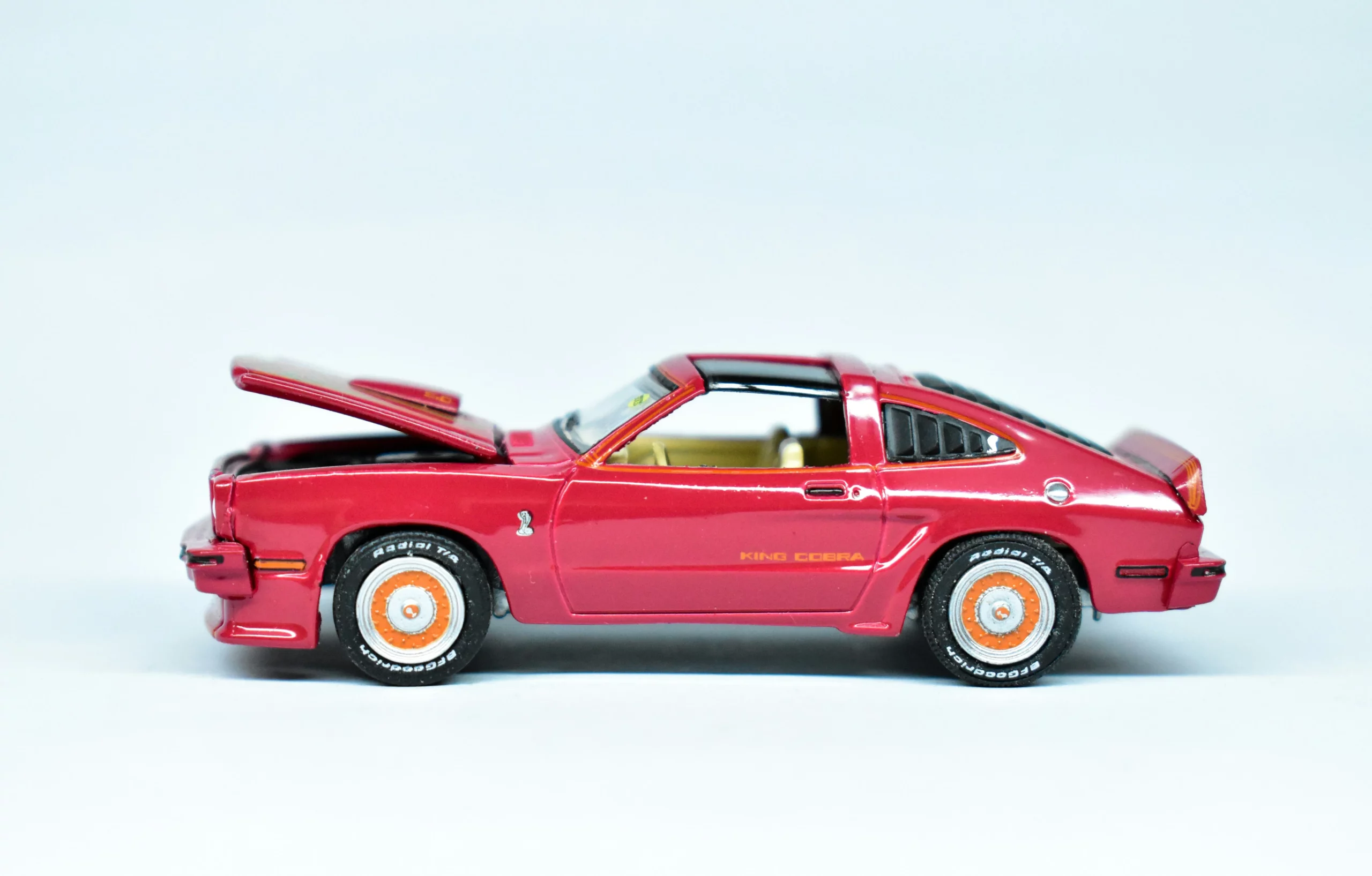 A red model car collection item with the hood open. The background is a very pale blue.