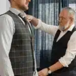 a man wearing a tweed vest suit is being measured by a tailor for american sizes in germany