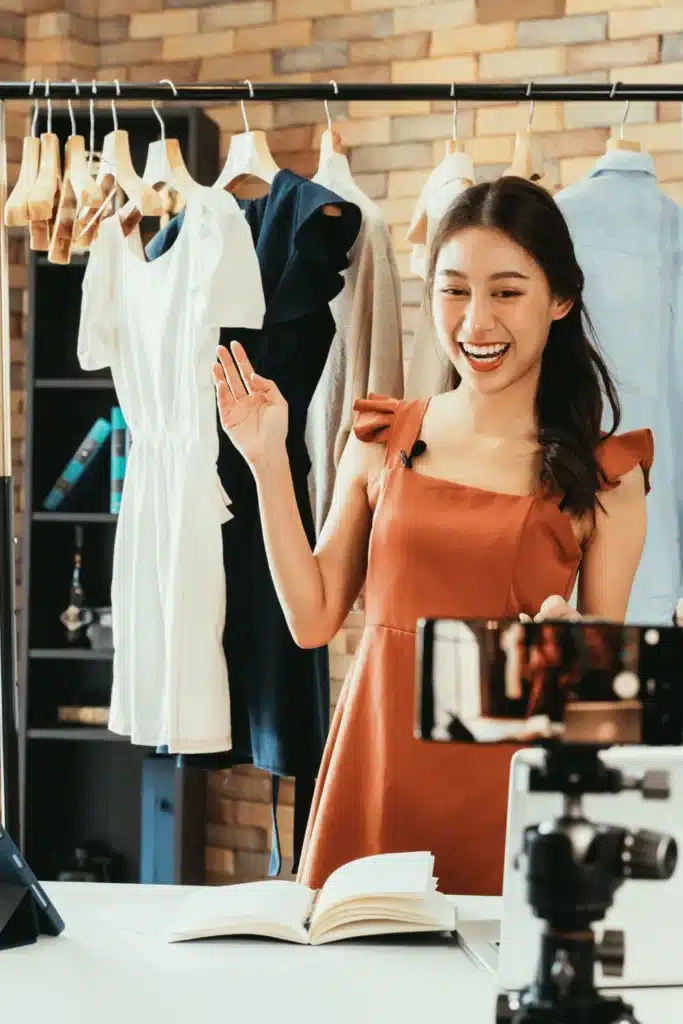 a woman is shopping for american clothes in asian sizes, so she needs to convert asia size to us first for the best fit. she is smiling in front of a clothing rack. 