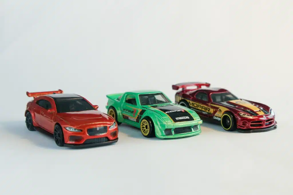 a model car collection of three cars: a red one with a spoiler is on the left, a green one in the middle, and another one is red with a stripe design on the right. 