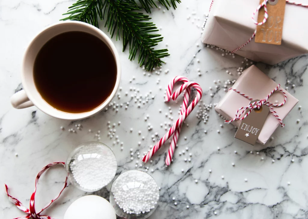 Canady canes, pine, hot chocolate and a small present on a marble countertop.