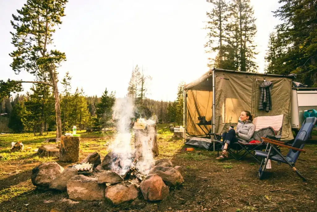 Someone is camping in a tent, with a lit bonfire outside. It's still sunny.