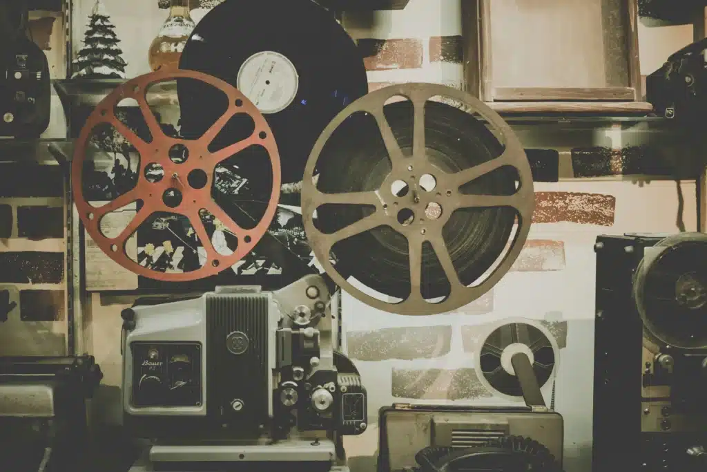 A projector with reels of film attached to it. In the room, there are other older media tools as well.