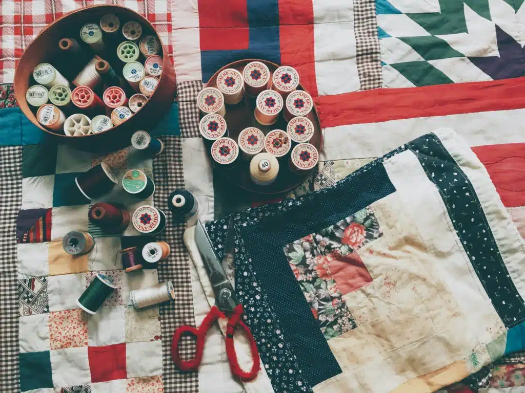 Pieces of quilted fabric and spools of thread show the details put into cultural American gift ideas. Scissors lay on top.