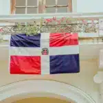 A Dominican flag hangs above a doorway outside of a building. This is the featured image for our blog post, answering, "does Amazon Deliver to Dominican Republic"?