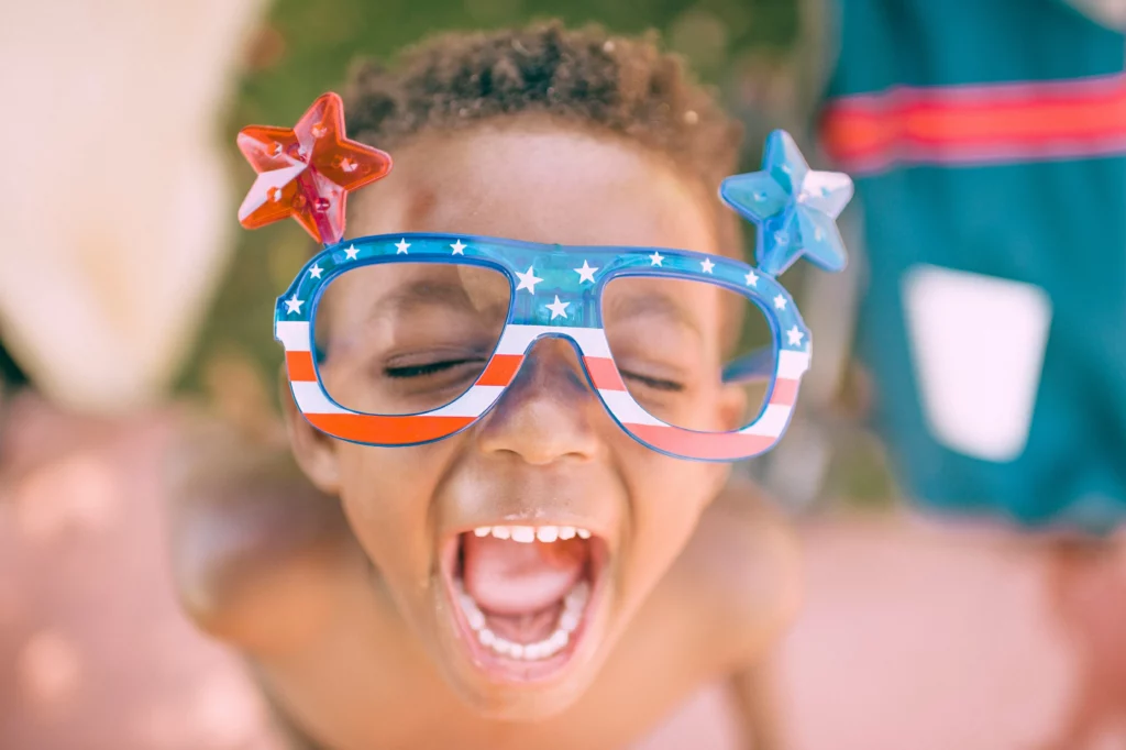 A happy child with large plastic glasses adorned in a pattern resembling the US flag.