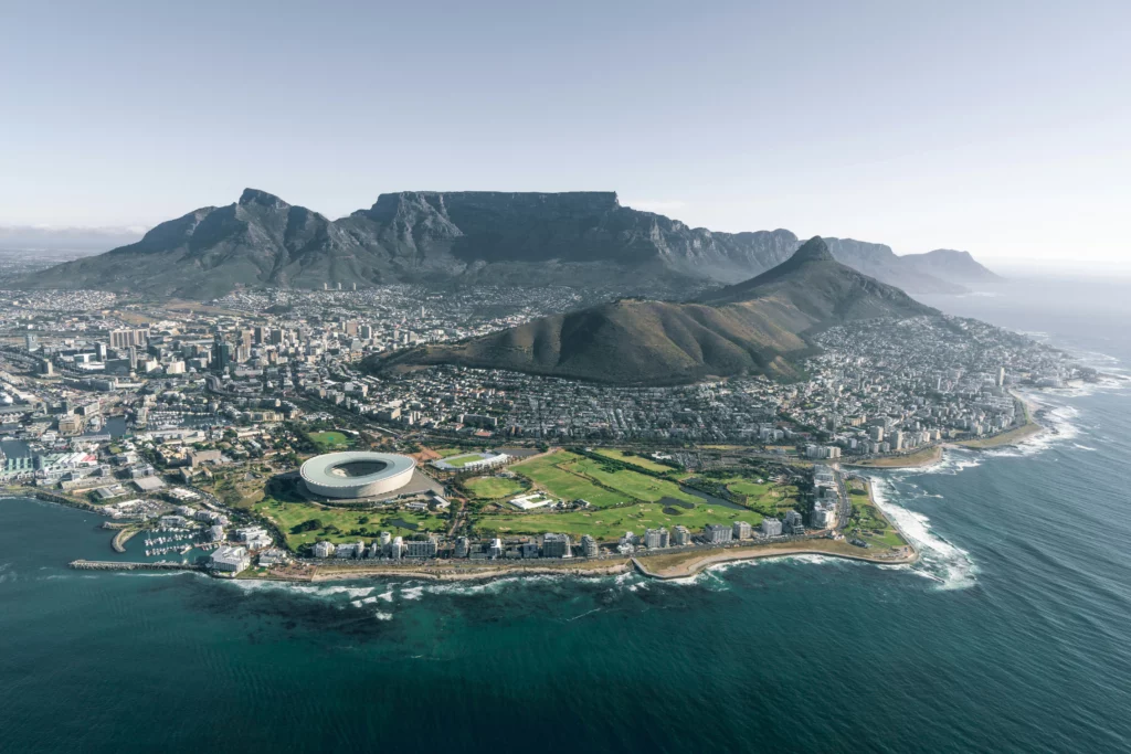 A coastal town in South Africa is seen from a helicopter or plane. On the left side is a port from shipping from USA to South Africa. In the front, there are beaches.