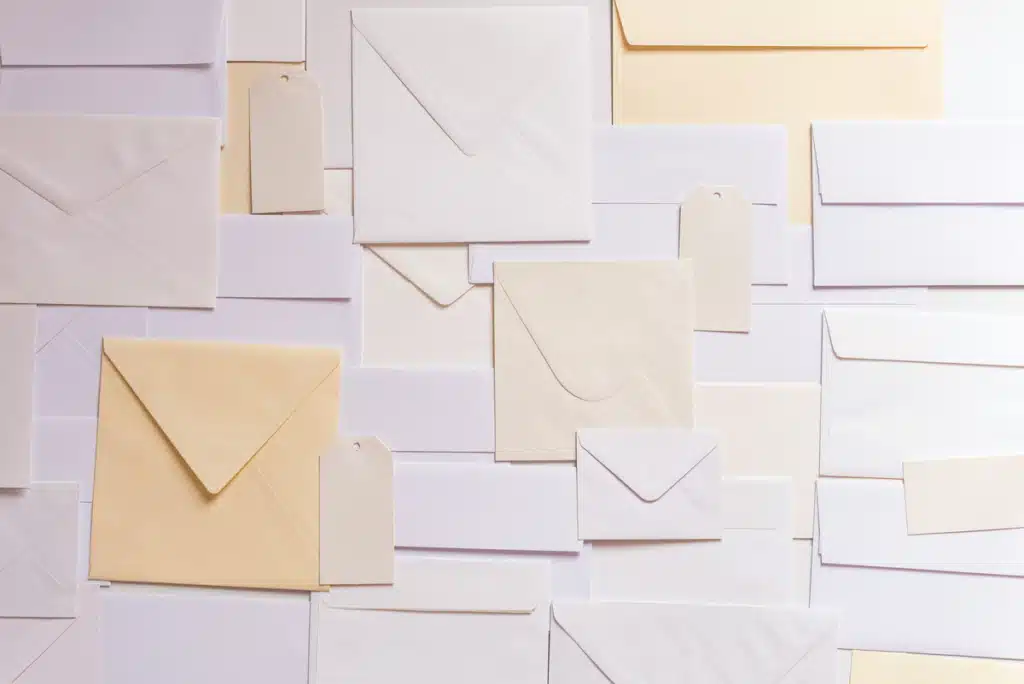 Layers of white and off-white envelopes cover a flat surface. Those expecting this many deliveries may be wondering, "what time does the mail run in my area?"