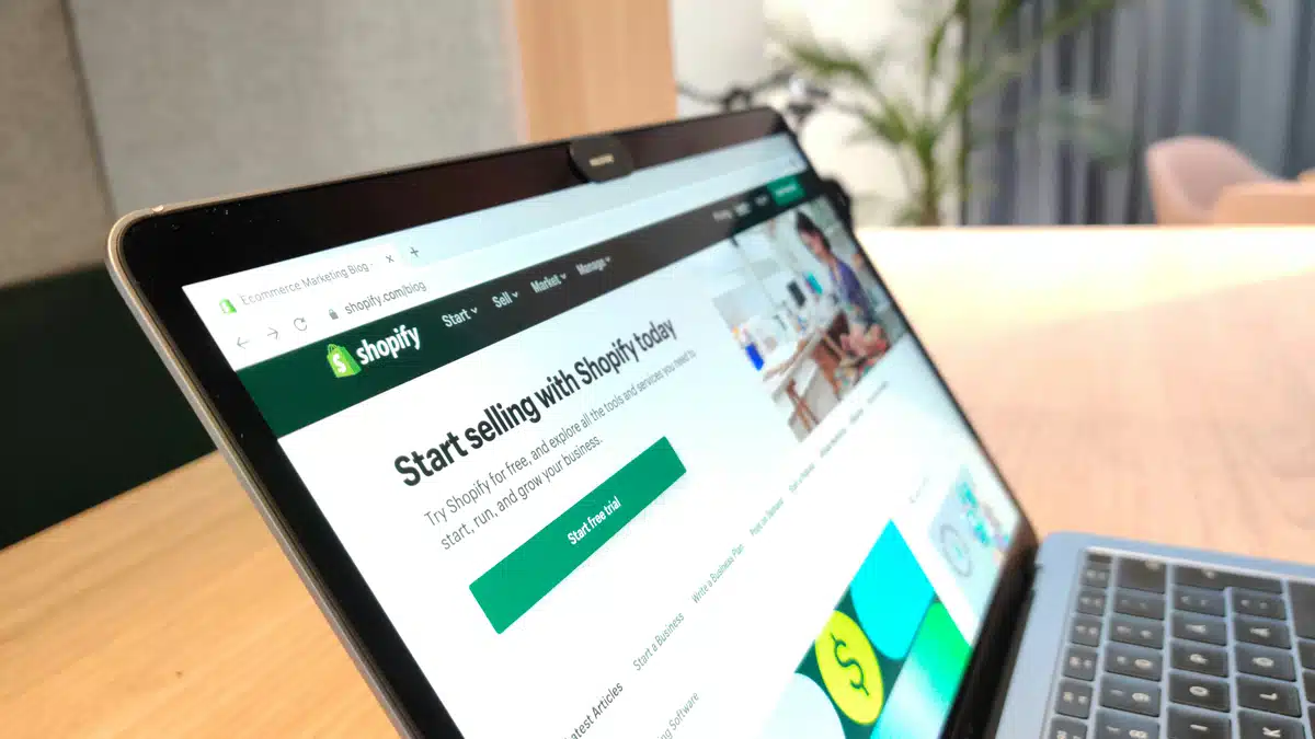 Someone has Shopify open on their Laptop, which is on a desk in a sunny room. They are managing an online shop that requires ecommerce shipping.
