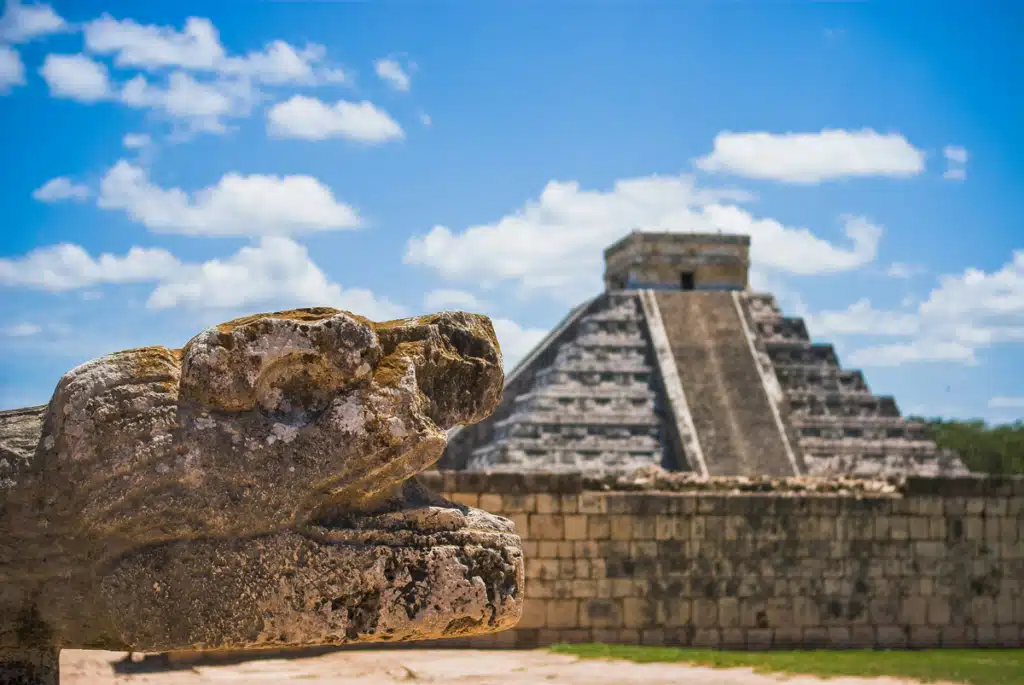Una rovina messicana frequentata dai turisti, che assomiglia a una piramide di pietra. In primo piano una formazione rocciosa. Il cielo è azzurro e parzialmente nuvoloso.
